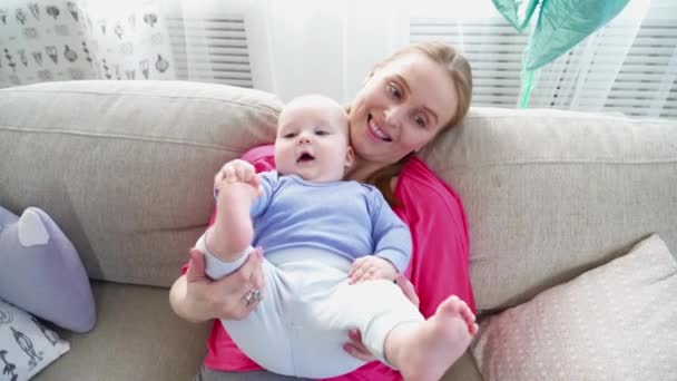 Bonita mãe brincando com seus 6 meses filhos pernas deitadas no sofá — Vídeo de Stock