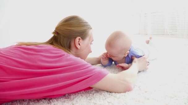 Joven madre ayudando a su hijo de 6 meses a arrastrarse por el suelo, primer paso — Vídeo de stock