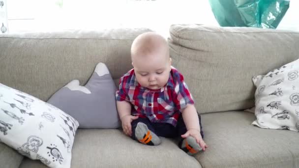 Маленький милый мальчик сидит и смотрит вокруг на диван — стоковое видео
