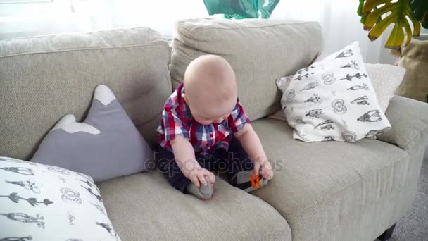 Маленький милый мальчик сидит на диване и играет ногами — стоковое видео