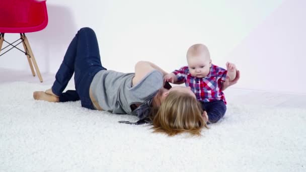 Młoda matka układanie na dywanie, gry z jej syn zwolnionym tempie — Wideo stockowe
