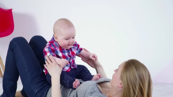 Young mother laying on the carpet playing with her son sitting on her slow motion — Stock Video