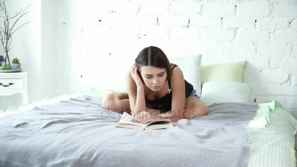 Belle femme assise sur le lit en pose de lotus et lisant un livre — Video