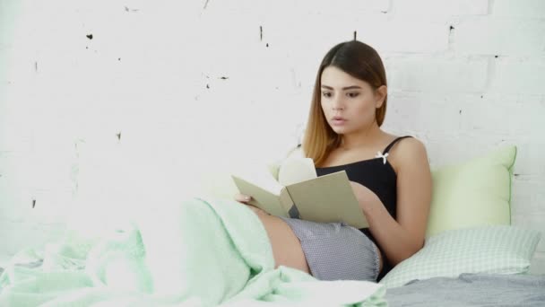 Joven hermosa mujer sentada en la cama y leyendo un libro — Vídeos de Stock