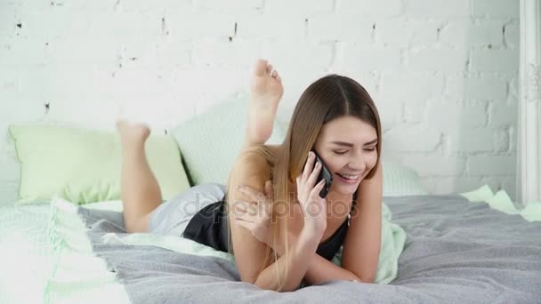 Mujer joven acostada en la cama y hablando por teléfono — Vídeos de Stock