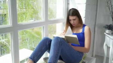 Pencere pervazına üzerinde oturan ve bir kitap okuma genç güzel kadın