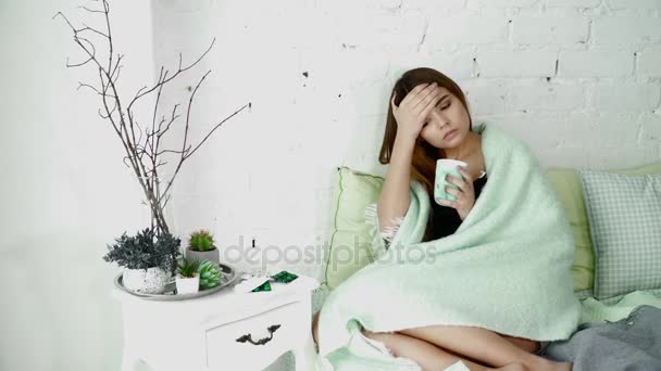 Mujer joven enferma en la cama debajo de la manta con té caliente — Vídeos de Stock