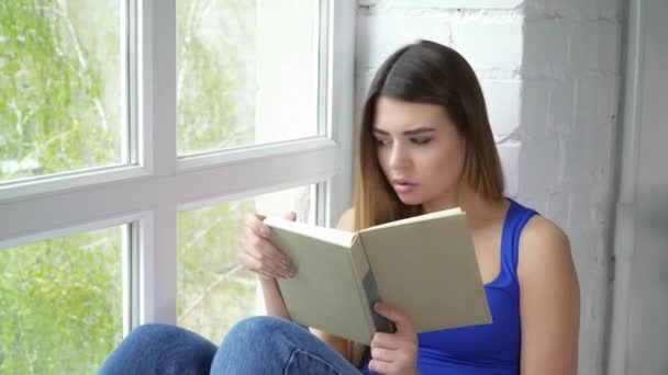 Jeune femme assise sur le rebord de la fenêtre et lisant un livre gros plan — Video