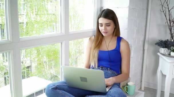 Młoda brunetka kobieta za pomocą laptopa, rozmowy na skype, siedząc na parapecie — Wideo stockowe