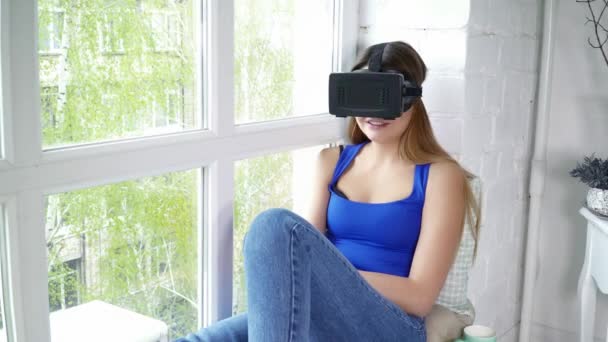 Νεαρή γυναίκα κάθεται στο περβάζι του παραθύρου και χρησιμοποιώντας closeup γυαλιά εικονικής πραγματικότητας — Αρχείο Βίντεο