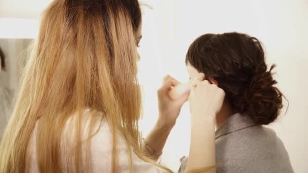 Young makeup artist applying base with brush to the young womans face — Stock Video