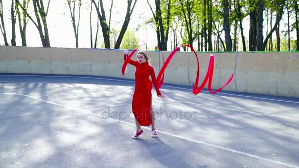 Mujer joven en un vestido rojo bailando con la cinta en el campo de cámara lenta — Vídeos de Stock