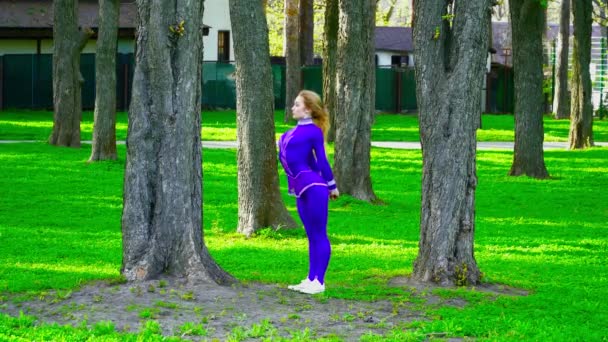 Joven gimnasta en traje violeta bailando y haciendo trucos en el parque — Vídeo de stock