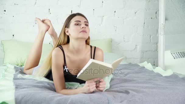 Young brunette woman reading a book on her bed and smiling — Stock Video