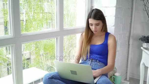 Mladá žena pomocí přenosného počítače sedí na detailním parapetu okna — Stock video