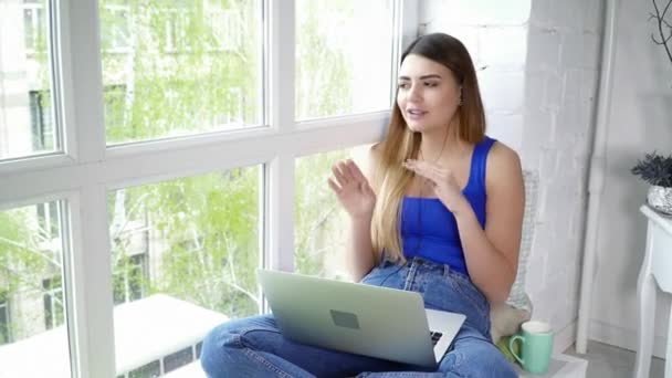 Mladá krásná žena, poslouchá hudbu a zpěv, sedí na okenním parapetu — Stock video