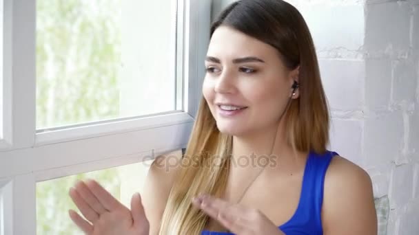 Mujer joven escuchando música y cantando sentada en el alféizar de la ventana — Vídeos de Stock