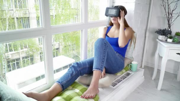 Mujer joven sentada en el alféizar de la ventana y usando gafas de realidad virtual — Vídeos de Stock