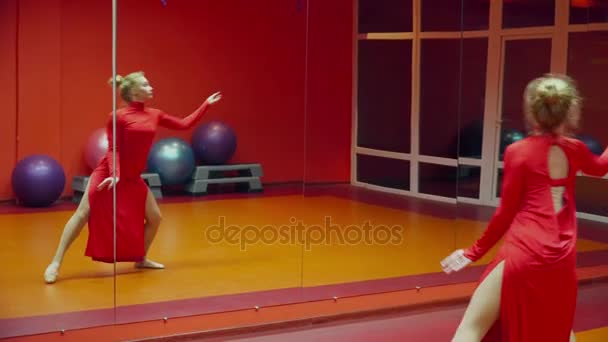 Νέος γυμναστής γυναίκα που χορεύει στην αίθουσα χορού σε ένα κόκκινο φόρεμα μπροστά από τον καθρέφτη — Αρχείο Βίντεο