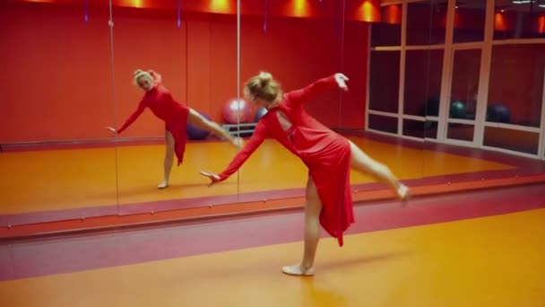 Jovem ginasta dançando na aula de dança em um vestido vermelho na frente do espelho — Vídeo de Stock