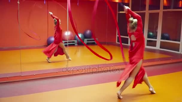 Joven hermosa gimnasta bailando con la cinta en la clase de baile en un vestido rojo — Vídeos de Stock