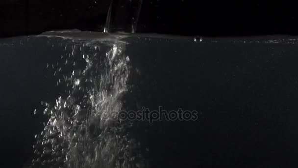 Nahaufnahme des Gießens von Wasser in Wasser auf schwarzem Hintergrund — Stockvideo