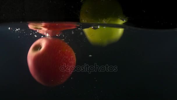 Gros plan de pommes vertes et rouges tombant dans l'eau sur le fond noir au ralenti — Video