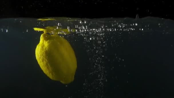 Gros plan d'un citron tombant dans l'eau sur fond noir au ralenti 