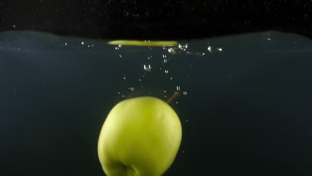 Close-up van verse smakelijke groene appel vallen in water op de zwarte backgrond slow motion — Stockvideo