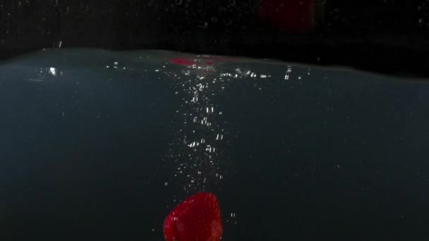 Närbild av jordgubbar som faller i vattnet på svart backgrond slow motion — Stockvideo