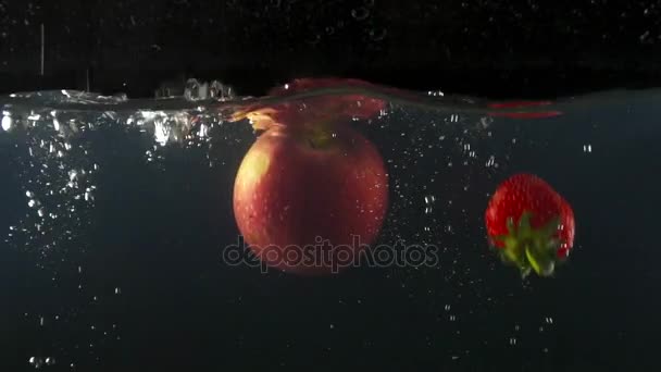 Closeup de maçã fresca e morangos caindo na água no fundo preto lento movimento — Vídeo de Stock