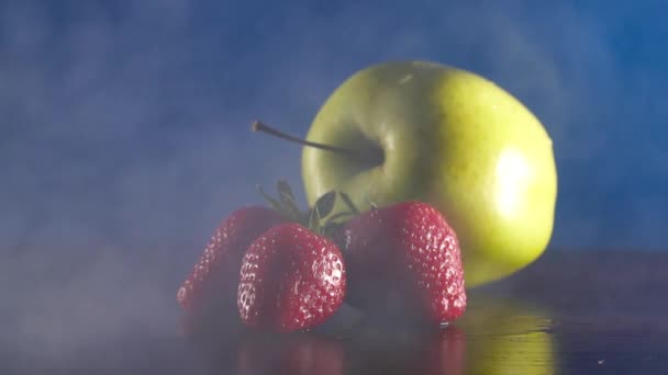 Biologische verse smakelijke apple en aardbeien in rook op de blauwe achtergrond — Stockvideo