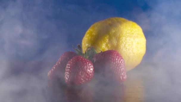 Bio-frische schmackhafte Zitrone und Erdbeeren in Rauch auf blauem Hintergrund — Stockvideo