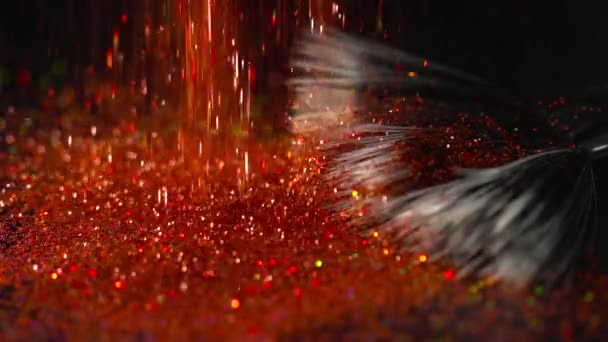 Brillos brillantes rojos que caen sobre el cepillo de maquillaje en el fondo negro, cámara lenta abstracta — Vídeos de Stock