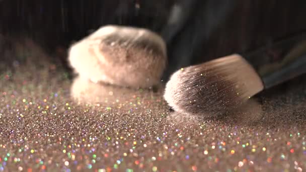 Paillettes dorées tombant sur des pinceaux de maquillage sur le fond noir, ralenti abstrait — Video