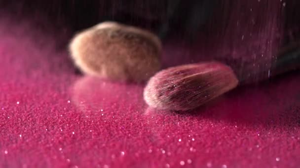 Roze glitter vallen op de make-up borstels tegen de zwarte achtergrond, abstract Slowmotion — Stockvideo