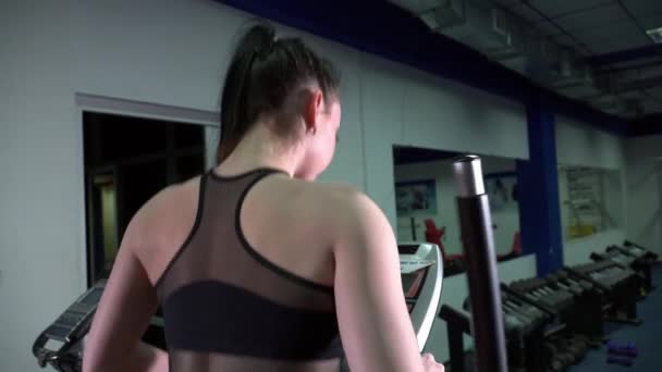 Jonge vrouw runing op de elliptische uitzicht vanaf de achterkant — Stockvideo