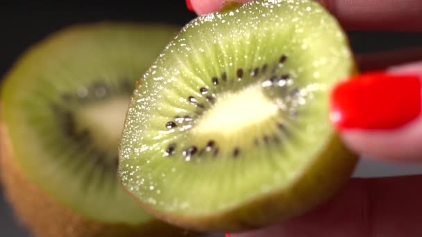 Nahaufnahme der aufgeschnittenen Kiwi auf schwarzem Hintergrund in Frauenhand — Stockvideo