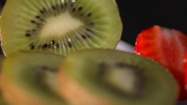 Closeup of sliced kiwi and strawberry on the black background slow motion — Stock Video