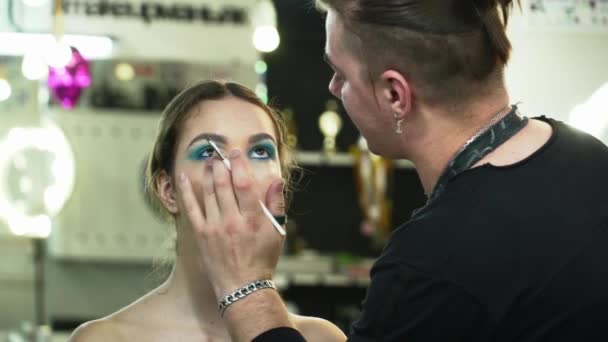 Художник грима делает лицо с синими тенями для молодой женщины в студии крупным планом — стоковое видео