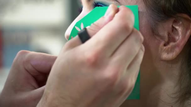 Maquillaje artista haciendo arte de la cara con una plantilla para una mujer primer plano — Vídeo de stock
