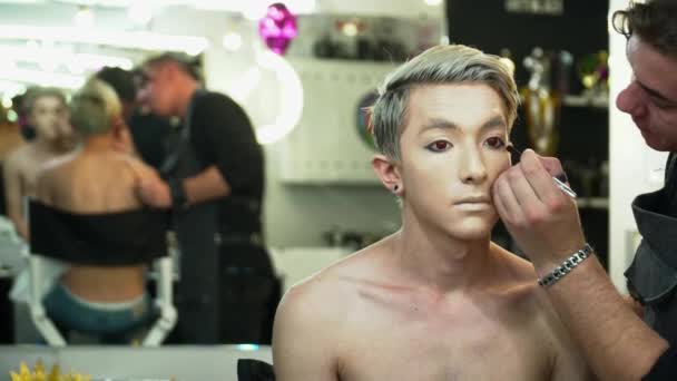 Maquillaje artista haciendo arte de la cara para un hombre joven delante del espejo — Vídeo de stock