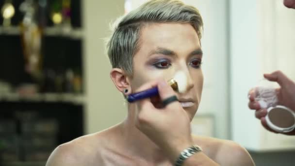 Make-up Artist macht Gesicht Art für einen jungen blonden Mann mit einem Make-up Pinsel Nahaufnahme — Stockvideo