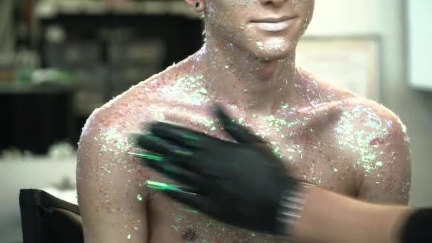 Художник макияжа покрывает тело молодого человека сверкающим крупным планом — стоковое видео
