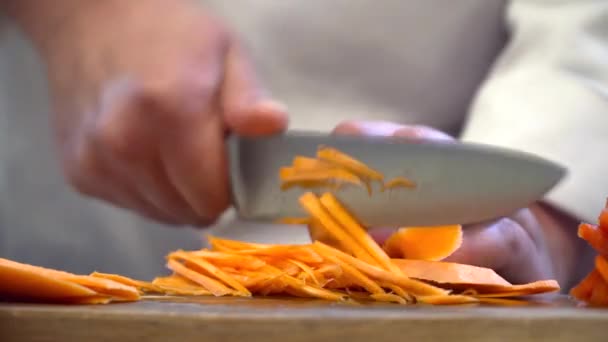 Шеф-повар режет морковку ножом на доске — стоковое видео