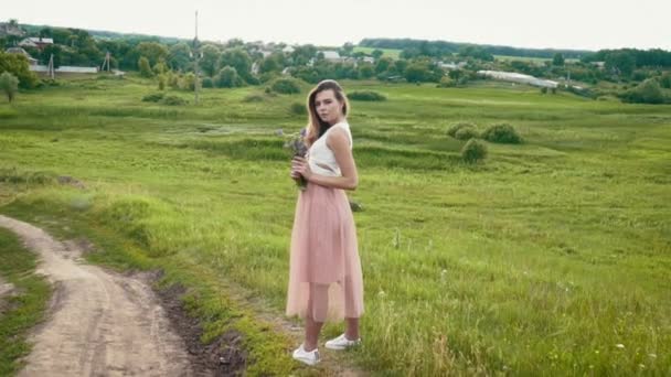 Beautiful young woman on the meadow with wild flowers in her hands slow motion — Stock Video