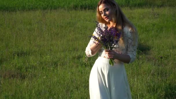 Beautiful young woman in white dress gathering flowers on the meadow slow motion — Stock Video