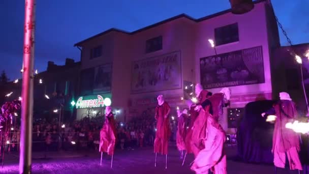 Stilt walkers ger eld facklor till man i svart och kvinna i vitt. — Stockvideo