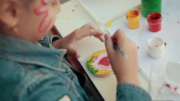 소녀는 붓을 사용하여 빨간색, 흰색, 초록색, 노란색으로 마음을 그리고 있다. — 비디오