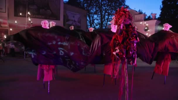 Female stilt walkers tied with one black piece of fabric dance in circle. — Stock Video